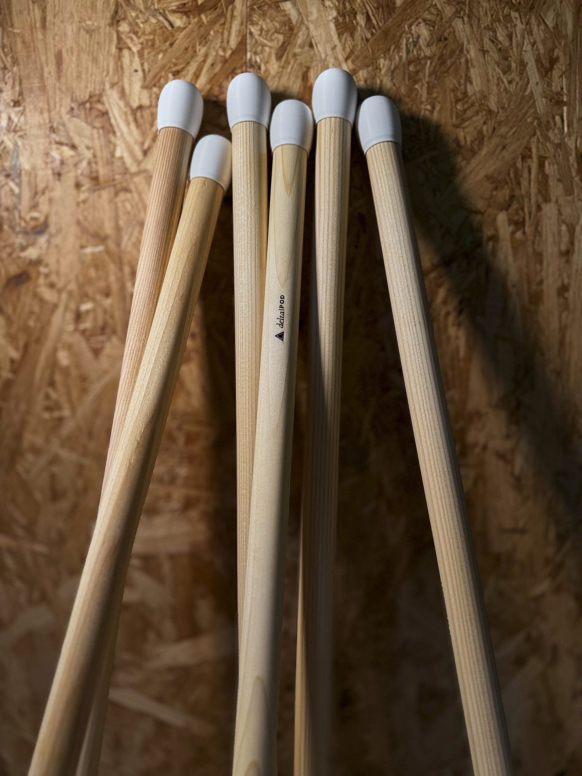 Mehrere delta·POD Holzbeine mit weißen PLA-Endkappen, eines mit eingebrannter Logo-Gravur, in der Werkstatt